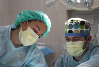 Locum surgeon and nurse managing a post-surgical patient in the ICU, wearing disposable gowns, surgical masks, and hair covers.